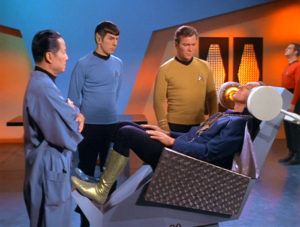 Kirk, Spock,and Governor Corey stand over Garth in the mental health chair