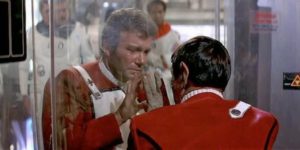 Kirk outside the radiation chamber, where Spock is dying. Their hands are pressed against opposite sides of the glass. Kirk's face is anguished and tear-streaked.
