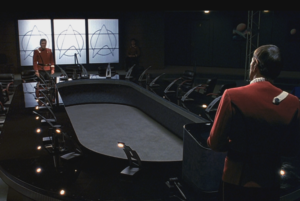 Spock and Kirk face each other from opposite ends of a conference table.